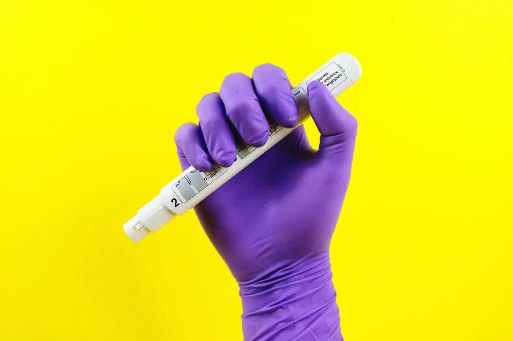 Purple-gloved hand holing an adrenaline auto-injector preparing to administeradrenaline